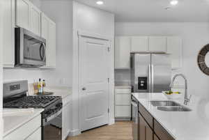 Dual tone kitchen featuring stainless steel appliances, light wood-type flooring, two tone cabinets, and light stone counters