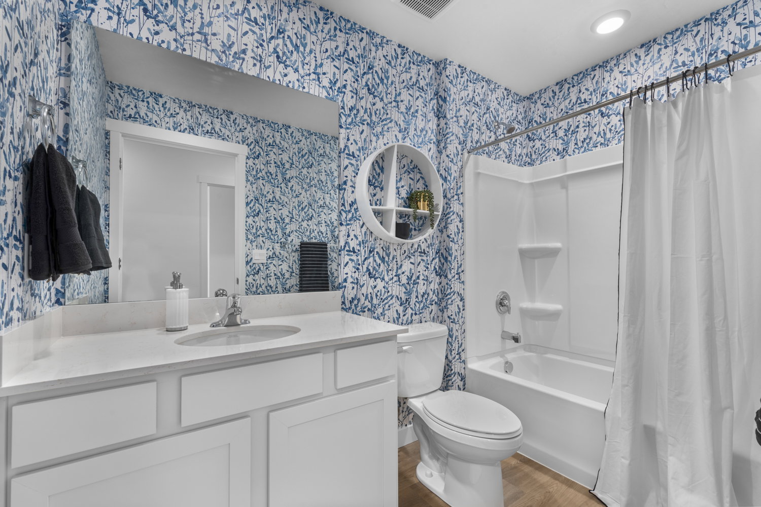 Bathroom featuring vanity, shower / bathtub combination with curtain, light wood finished floors, and wallpapered walls