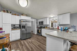 Kitchen featuring a peninsula, a kitchen bar, stainless steel appliances, white cabinets, and light countertops