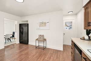 Kitchen featuring light countertops, black fridge, stainless steel dishwasher, light wood-like floors, and wood finish cabinets
