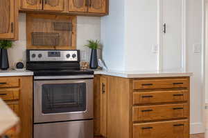 Kitchen featuring stainless steel range with electric stovetop, wood finish cabinetry, and light countertops