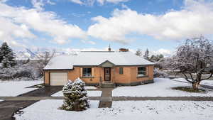 View of front of home with a garage, a chimney, brick siding, and driveway
