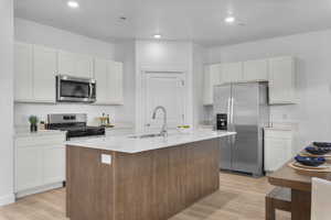 Kitchen with stainless steel appliances, an island with sink, light wood-type flooring, light stone counters, and recessed lighting