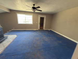 Unfurnished living room featuring a wood stove, carpet floors, a ceiling fan, and a textured ceiling