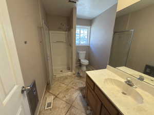 Bathroom with vanity, a shower stall, a textured ceiling, and light tile patterned floors