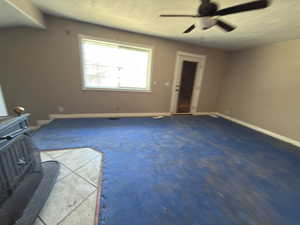 Unfurnished living room featuring a wood stove, carpet, and a ceiling fan