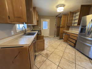 Kitchen featuring wood finish cabinets, light countertops, stainless steel appliances, a textured ceiling, and light tile patterned floors