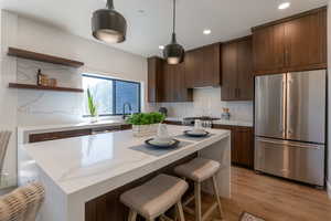 Kitchen featuring stainless steel appliances, light wood-style floors, a kitchen bar, open shelves, and dark wood finish cabinets