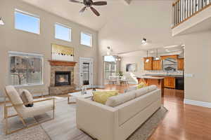 Living area featuring a fireplace, ceiling fan, light wood-style flooring, and lofted ceiling