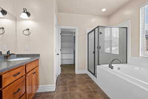 Bathroom with vanity, a spacious closet, a stall shower, a garden tub, and dark tile patterned floors