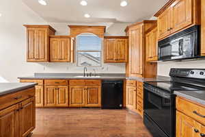 Kitchen featuring black appliances, dark wood-style flooring, wood finish cabinetry, and recessed lighting