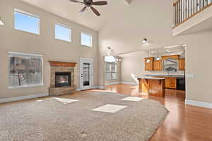 Unfurnished living room featuring a stone fireplace, light wood-style flooring, a ceiling fan, and a high ceiling