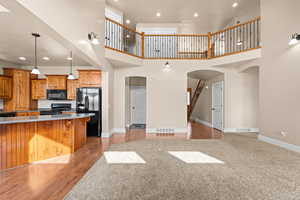 Kitchen featuring arched walkways, wood finish cabinets, black appliances, open floor plan, and decorative light fixtures