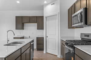 Kitchen with stainless steel appliances, light stone counters, dark wood finish cabinetry, light wood-style floors, and recessed lighting