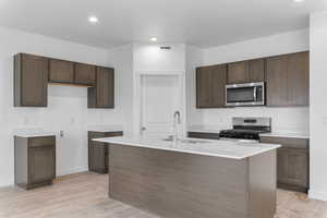 Kitchen with stainless steel appliances, a center island with sink, light wood-style flooring, recessed lighting, and light stone counters