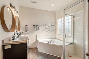 Bathroom with a bath, double vanity, a stall shower, dark wood finished floors, and recessed lighting
