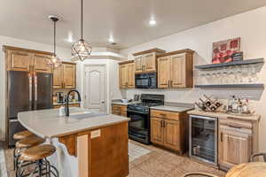 Kitchen with black appliances, wine cooler, a kitchen island with sink, pendant lighting, and a kitchen breakfast bar
