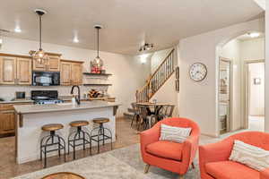 Kitchen with arched walkways, black appliances, a kitchen bar, a kitchen island with sink, and open shelves