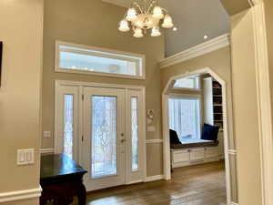 Foyer featuring a chandelier, light wood finished floors, healthy amount of natural light, and a high ceiling