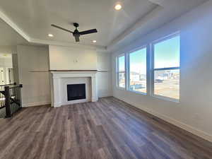 Unfurnished living room with a raised ceiling, a ceiling fan, dark wood-type flooring, a tiled fireplace, and recessed lighting