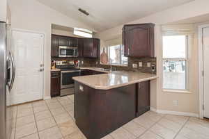 Kitchen with dark wood finish cabinetry, stainless steel appliances, lofted ceiling, a peninsula, and light tile patterned floors