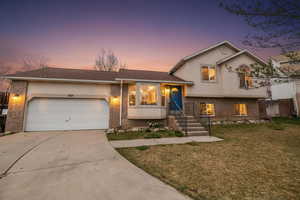 Tri-level home with brick siding, an attached garage, concrete driveway, and roof with shingles