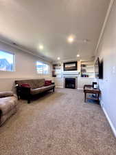 Living area with built in shelves, ornamental molding, carpet floors, a tile fireplace, and a textured ceiling
