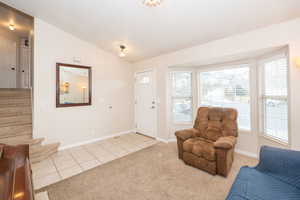 Foyer with vaulted ceiling, light colored carpet, and light tile patterned floors