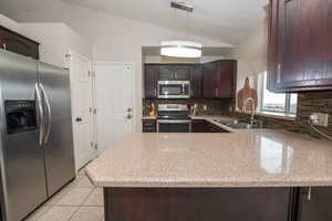 Kitchen featuring dark wood finish cabinets, stainless steel appliances, vaulted ceiling, decorative backsplash, and light tile patterned flooring