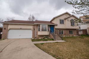 Split level home featuring brick siding, a garage, concrete driveway, and stucco siding