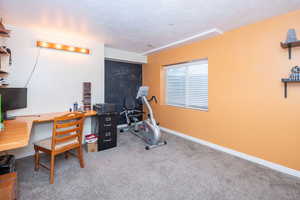Carpeted office space with a textured ceiling and baseboards