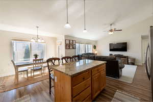 Kitchen featuring a kitchen breakfast bar, dark wood finished floors, light stone countertops, a center island, and hanging lights