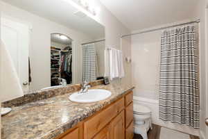 Full bathroom with a spacious closet, vanity, shower / bathtub combination with curtain, and light wood finished floors