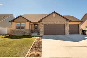View of front of property with an attached garage, concrete driveway, stone siding, and a shingled roof