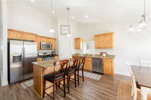 Kitchen featuring light stone countertops, stainless steel appliances, hanging lights, a kitchen breakfast bar, and light wood-style flooring