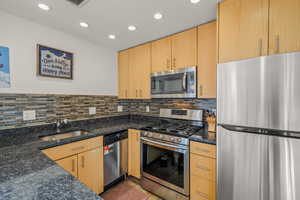 Kitchen featuring stainless steel appliances, light wood finish cabinets, dark stone counters, recessed lighting, and backsplash
