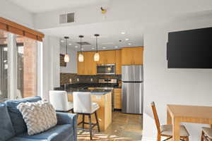 Kitchen featuring a kitchen bar, a peninsula, stainless steel appliances, dark stone countertops, and dark stone finish floors