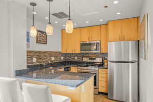 Kitchen featuring stainless steel appliances, a peninsula, dark stone countertops, a breakfast bar area, and decorative light fixtures