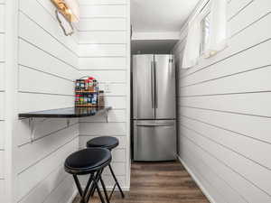 Kitchen with freestanding refrigerator, wooden walls, and dark wood-style flooring