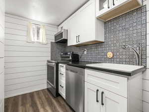 Kitchen featuring stainless steel appliances, white cabinetry, dark wood-style flooring, glass insert cabinets, and wood walls