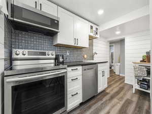 Kitchen featuring stainless steel appliances, white cabinetry, dark wood finished floors, recessed lighting, and glass insert cabinets