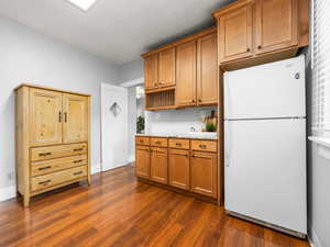 Kitchen with freestanding refrigerator, light countertops, wood finish cabinets, and dark wood-type flooring