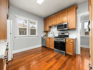 Kitchen featuring stainless steel appliances, wood finish cabinetry, dark wood-style floors, and light stone counters
