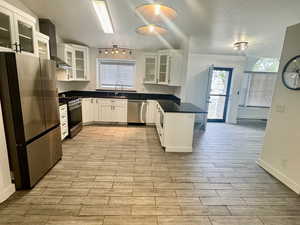Kitchen with glass insert cabinets, stainless steel appliances, dark countertops, a peninsula, and white cabinetry