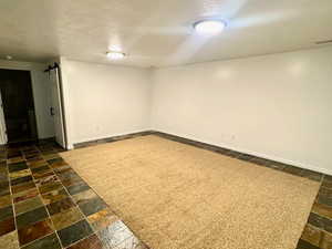 Finished basement with a textured ceiling and stone tile floors