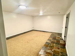 Finished basement with stone tile floors, a textured ceiling, and dark colored carpet