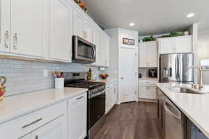 Two tone kitchen featuring stainless steel appliances, dark wood finished floors, backsplash, light stone countertops, and recessed lighting