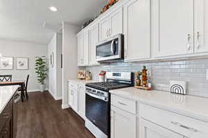 Kitchen with stainless steel appliances, white cabinets, dark wood finished floors, light stone counters, and a textured ceiling