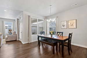 Dining area featuring a textured ceiling, dark wood-type flooring, healthy amount of natural light, and suspended lighting