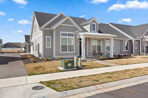 View of front of home with covered porch, roof with shingles, and a front yard